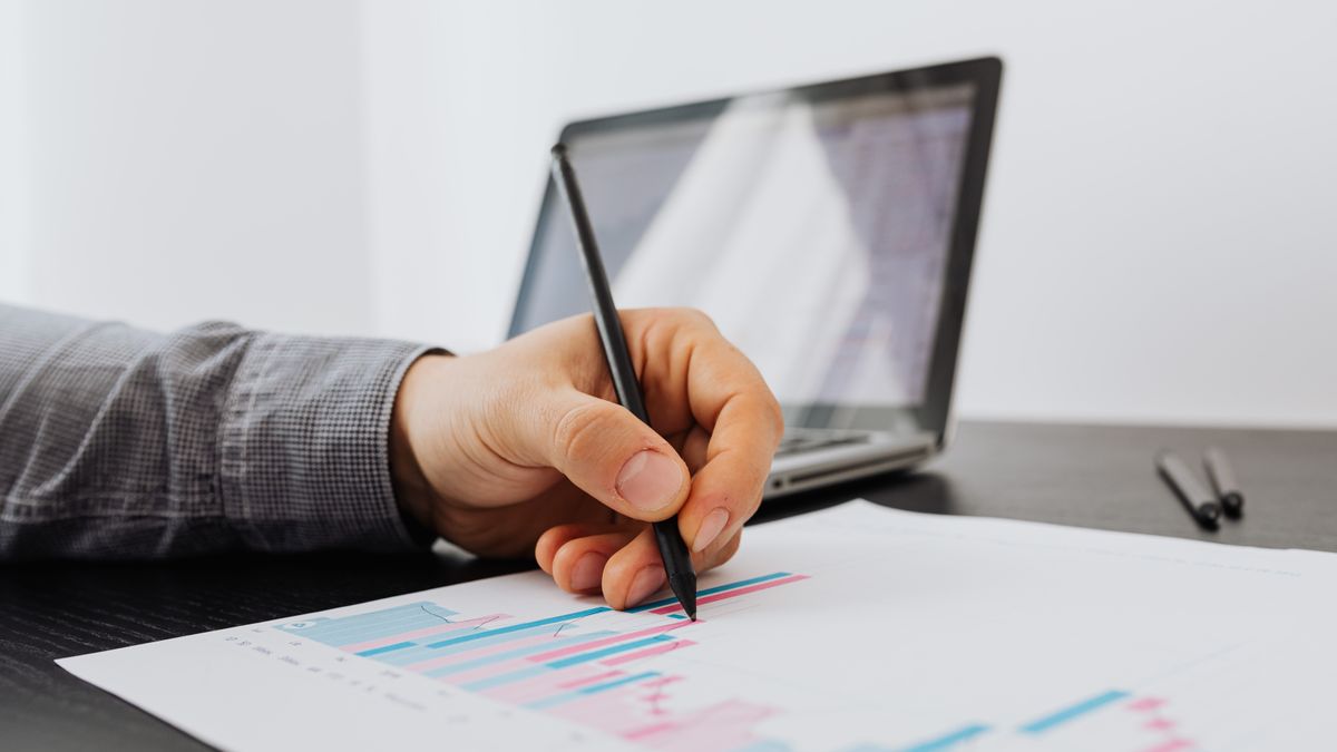 A hand reviewing a printed results chart beside a laptop, representing writing a case study that proves a client result and wins new clients.